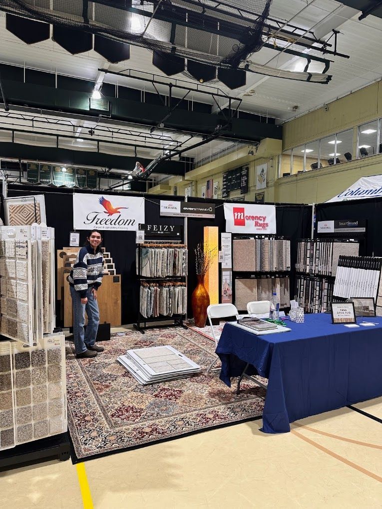Trade show booth with racks of clothing and hanging displays, staffed table draped in blue