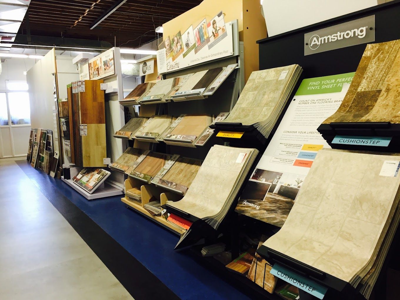 Wall display of flooring and tile samples in a showroom, with brochures and sample boards arranged on shelves.