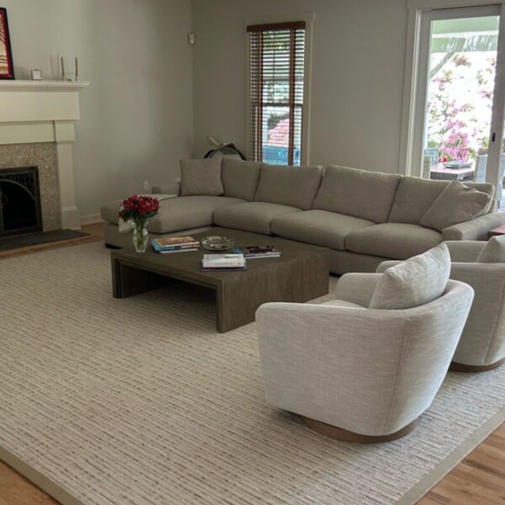 Bright living room with beige sectional sofa, white chair, coffee table, and fireplace on a woven rug