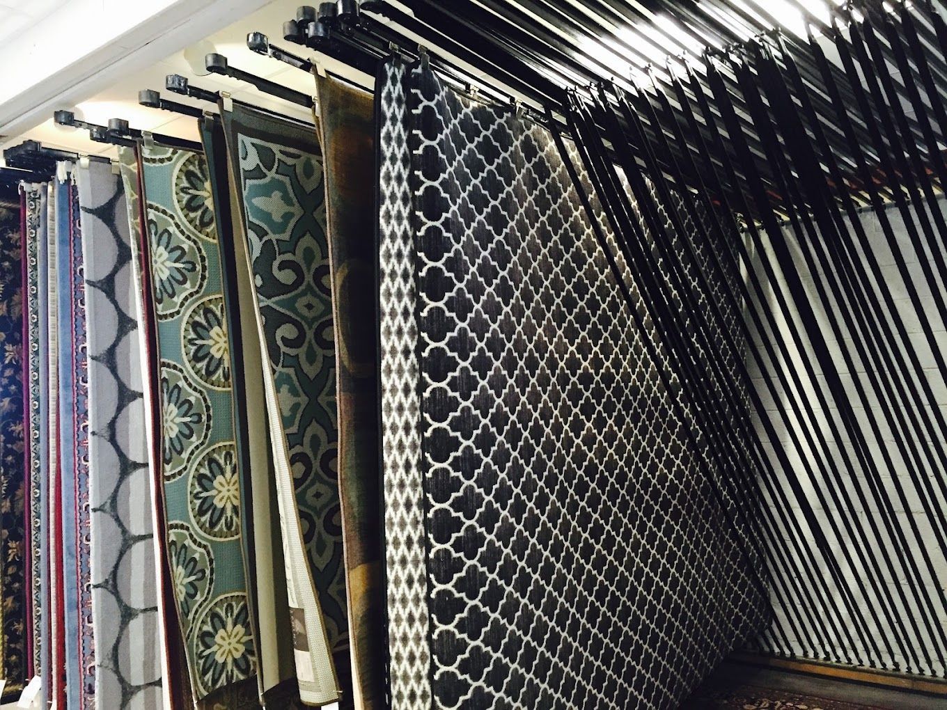 Rows of patterned hanging rugs or fabrics in assorted colors on display in a shop