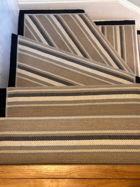 Stacked striped rugs in neutral tones leaning against a wall on a wooden floor.