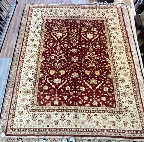 Red and cream patterned area rug with floral border on a wooden floor
