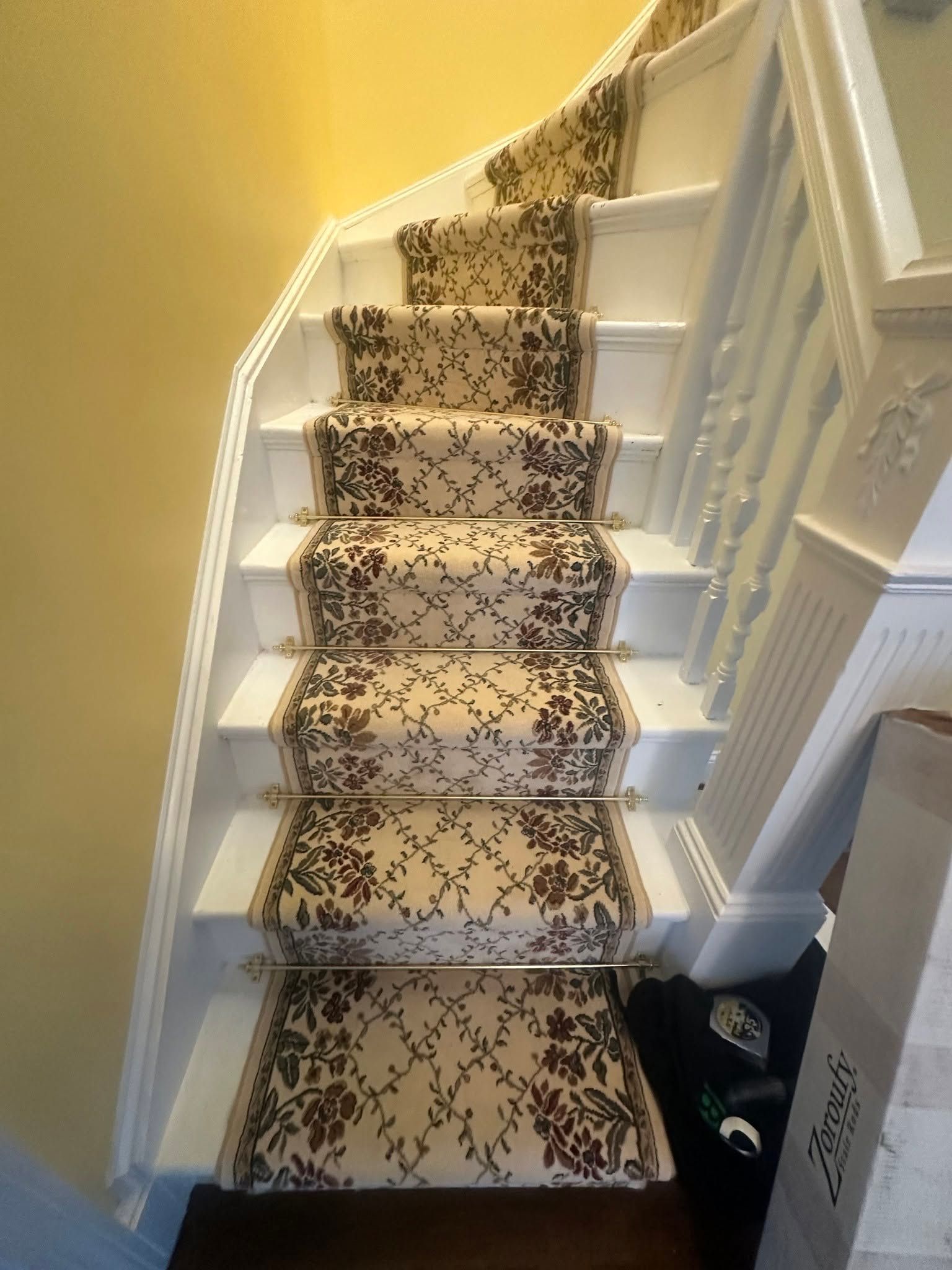 Carpeted staircase with patterned runner and white banister in a narrow hallway.