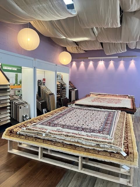 Oriental rugs displayed on raised racks in a purple-lit showroom with draped ceiling and hanging globe lights
