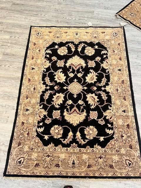 Beige and black patterned area rug with floral border on a light floor