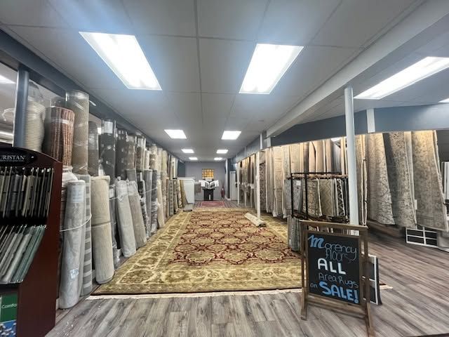 Carpet store aisle with rugs on both sides and a “All on sale” sign in front.