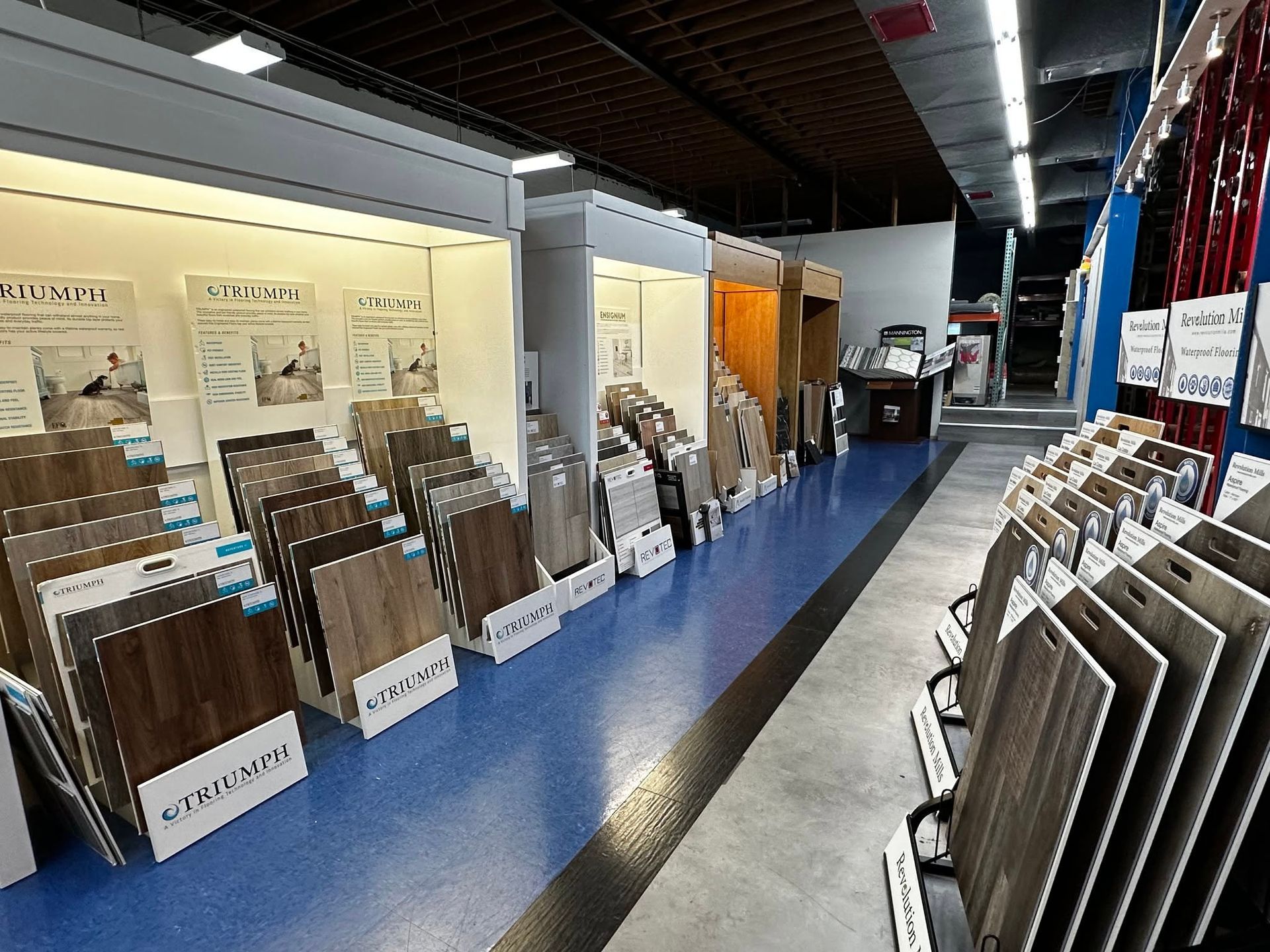 Long showroom aisle with display racks of wall tiles and flooring samples under bright lights