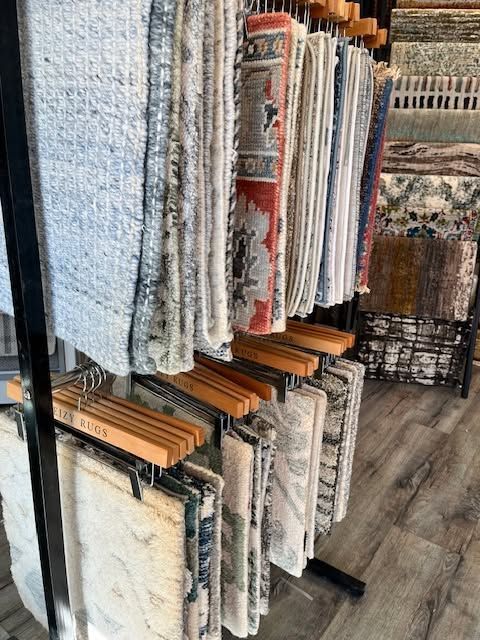 Display of rolled rugs and runners in a store, with patterned carpets hanging on metal racks.