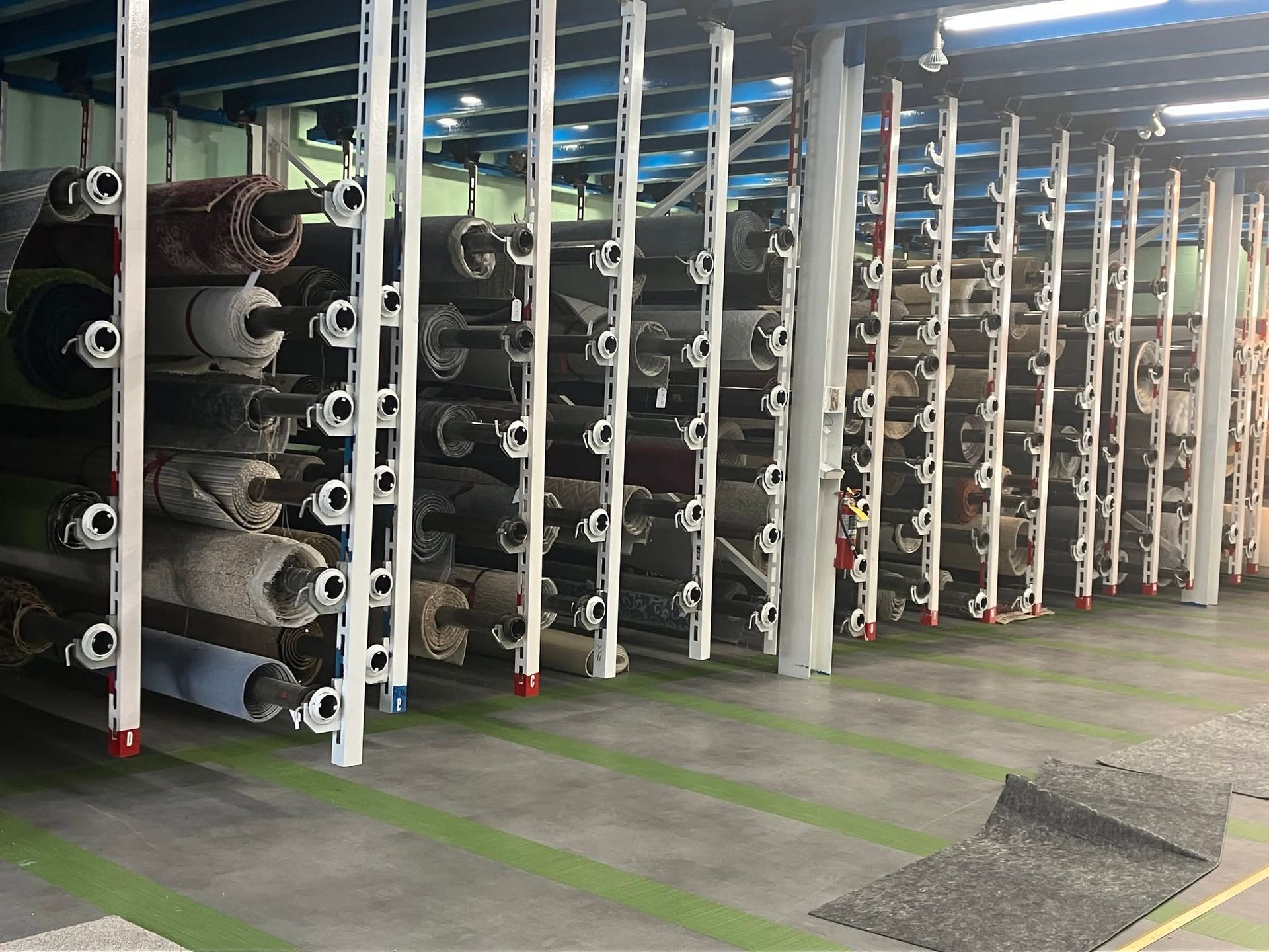 Rows of rolled carpets stacked on industrial racks in a warehouse-like storage area.