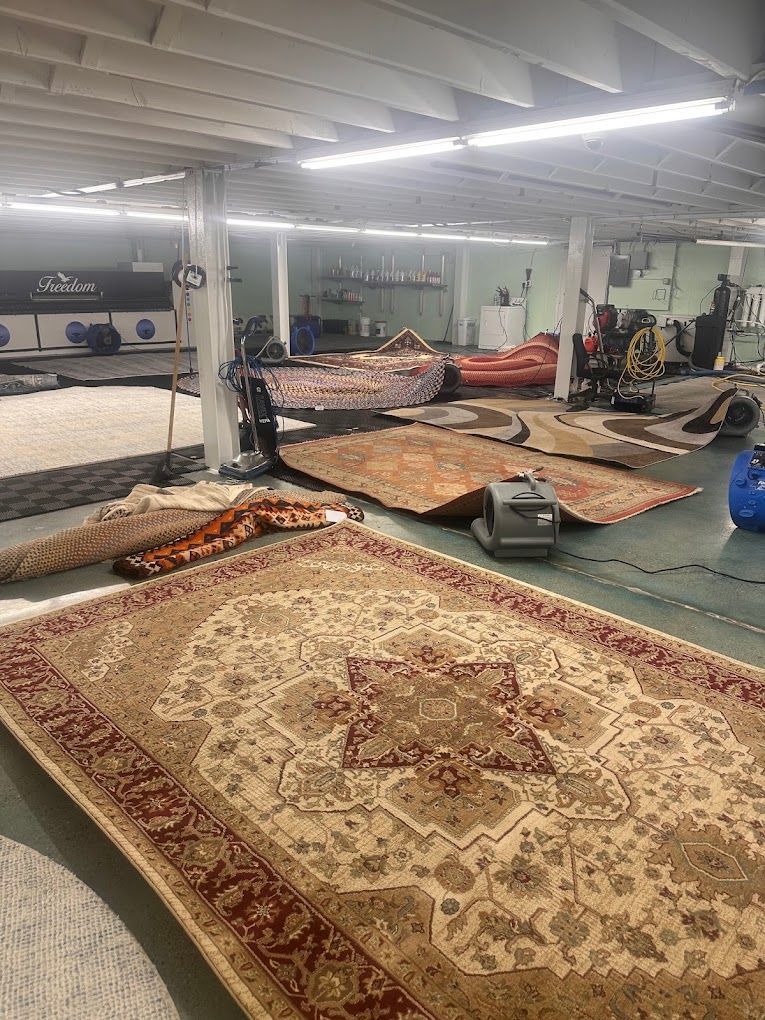 Rug store showroom with large patterned carpets, rolled rugs, and a carpet cleaner on the floor