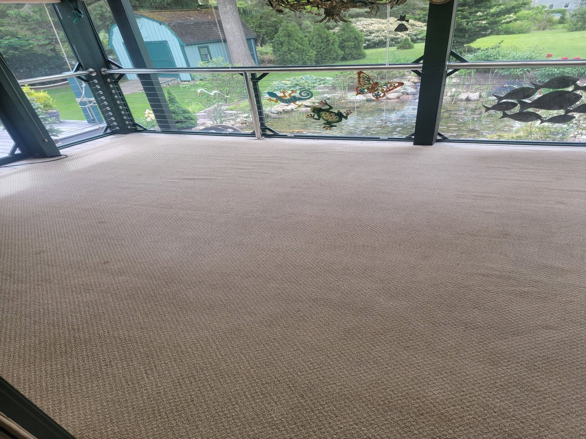 Empty carpeted room with large windows overlooking a garden and pond.
