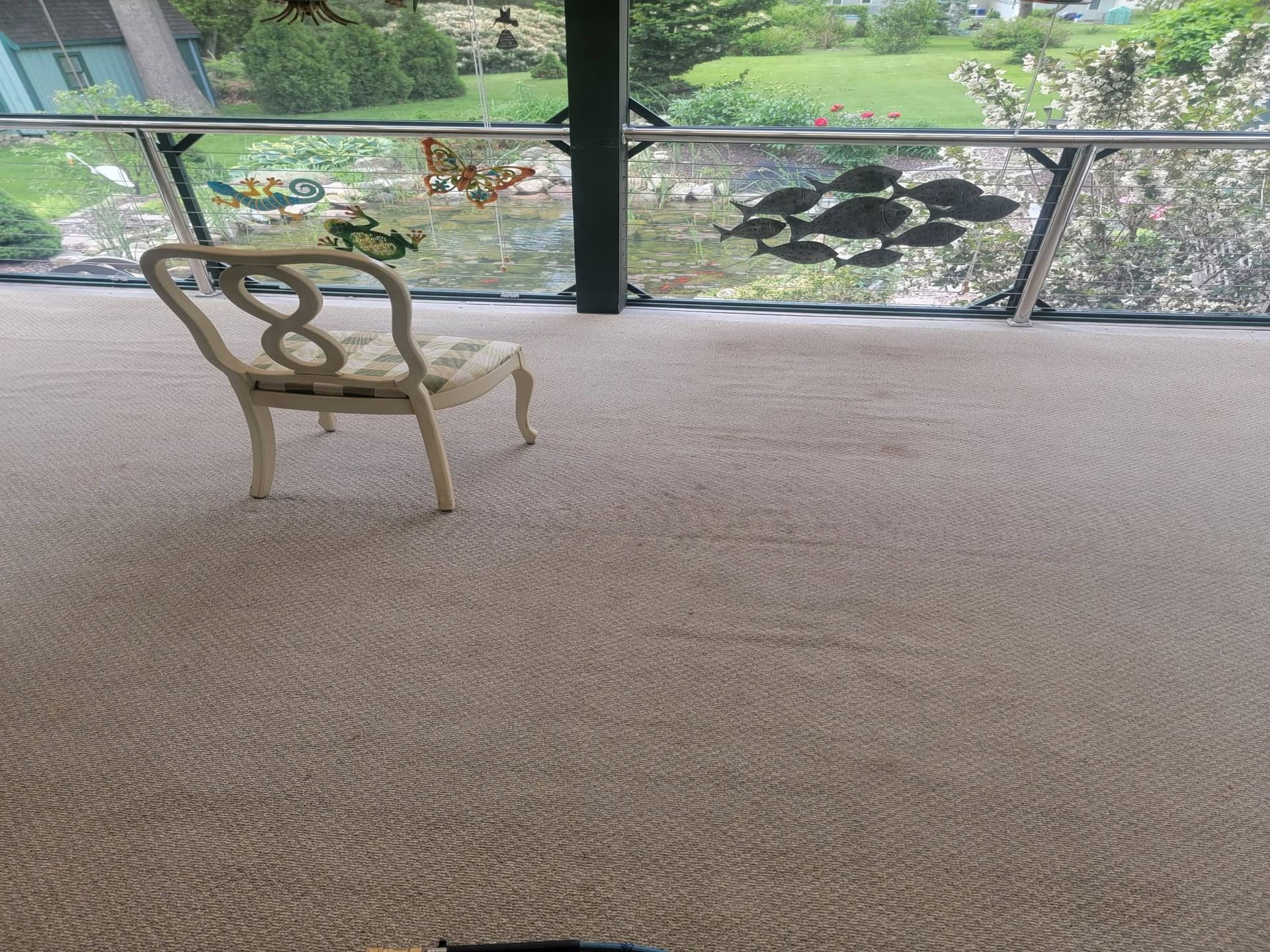 Empty chair on a carpeted patio overlooking a lush garden and pond beyond glass railing.