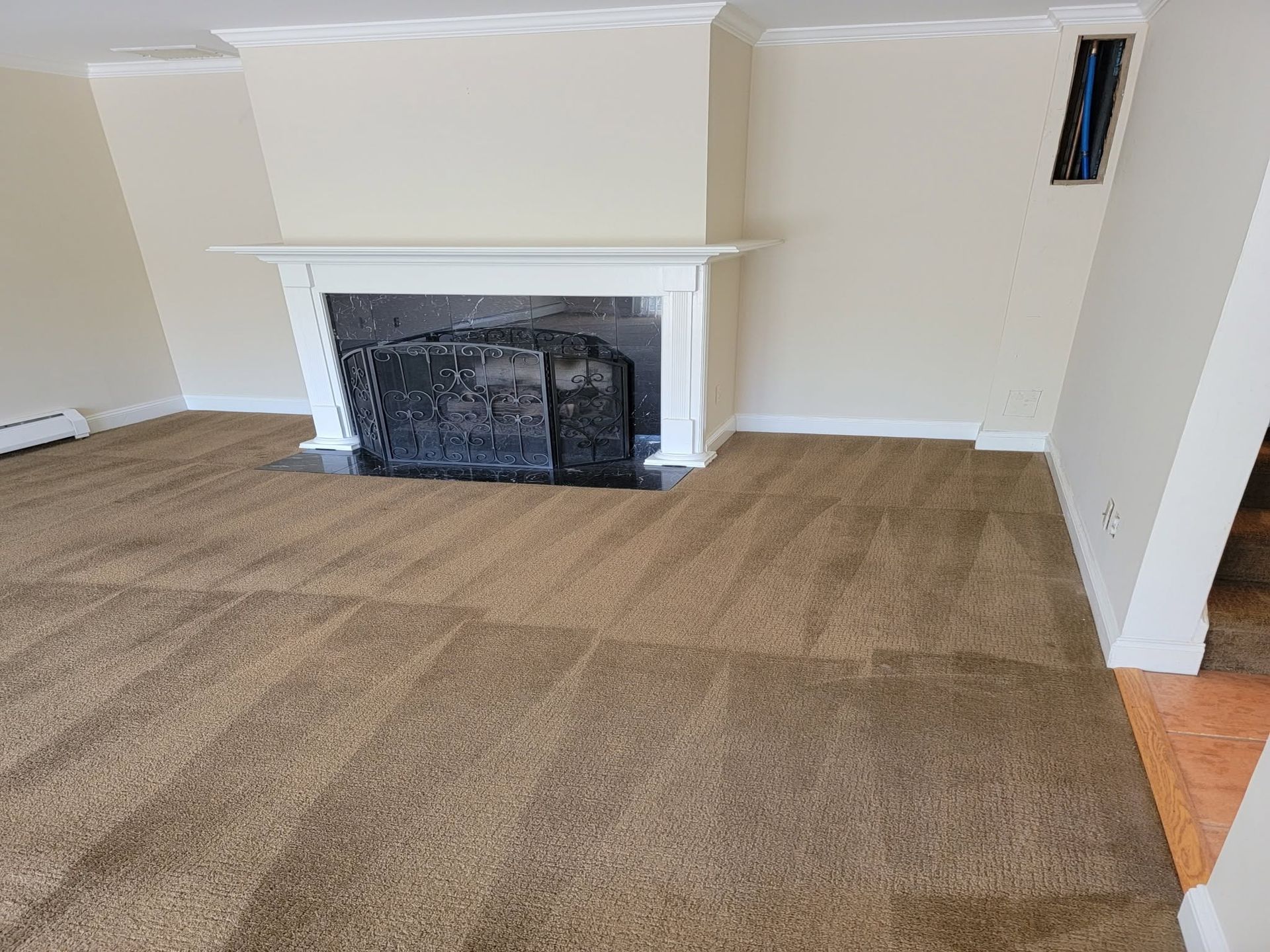 Empty living room with beige carpet and a white fireplace mantel on a cream wall.