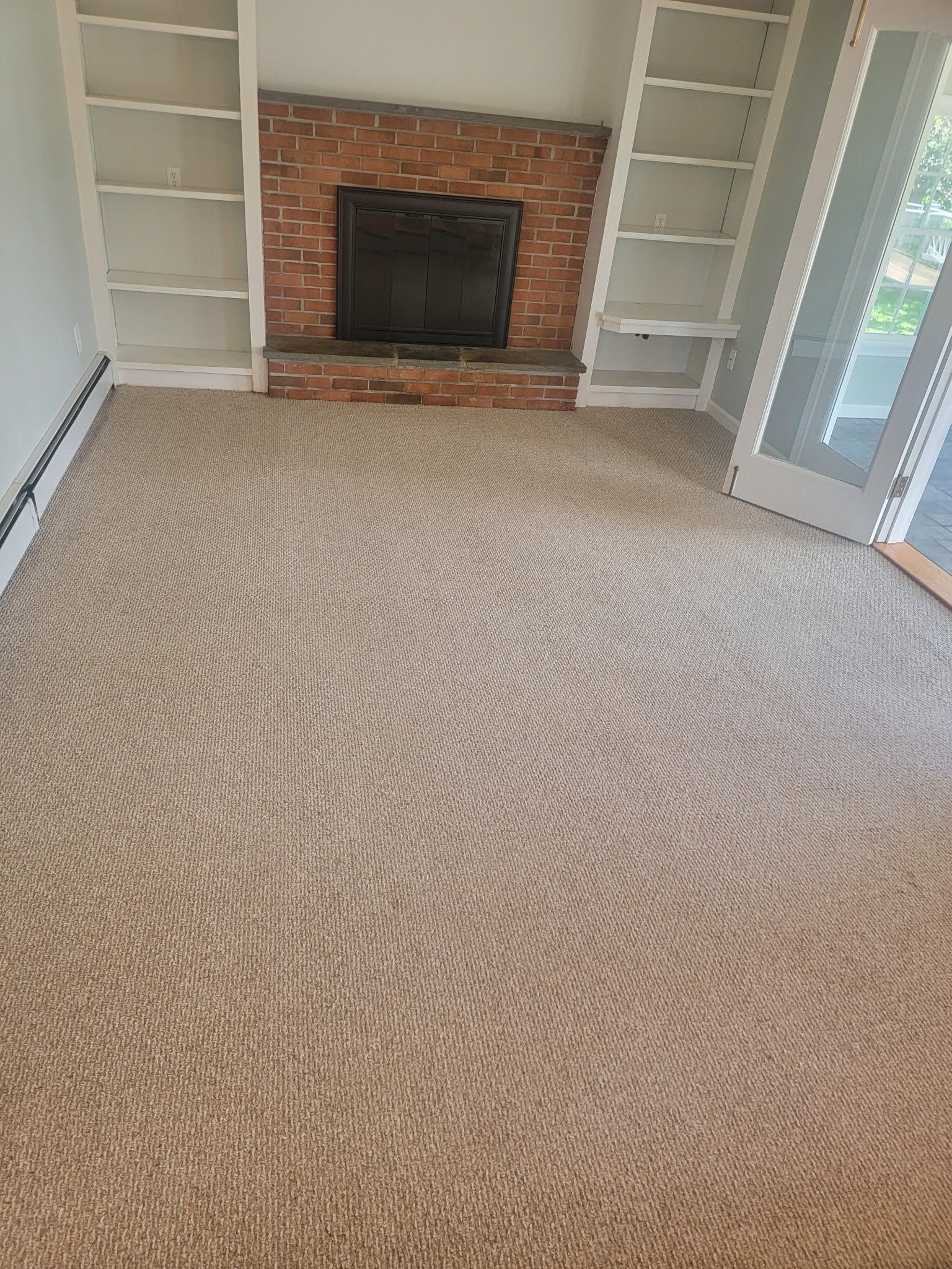 Empty living room with beige carpet, brick fireplace, and white built-in shelves on both sides.
