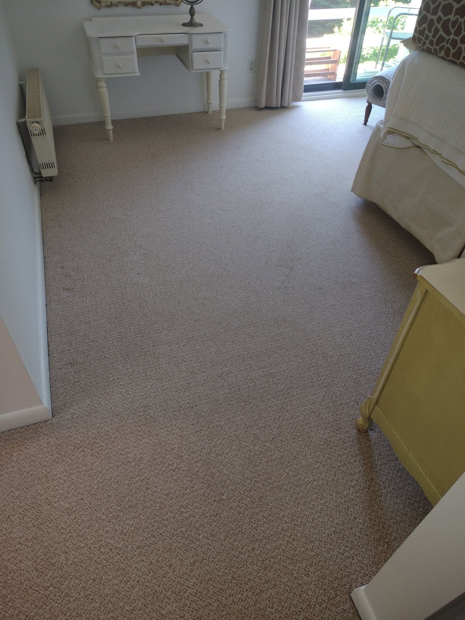 Carpeted bedroom with a vanity, bed, and open doorway to a bright balcony.