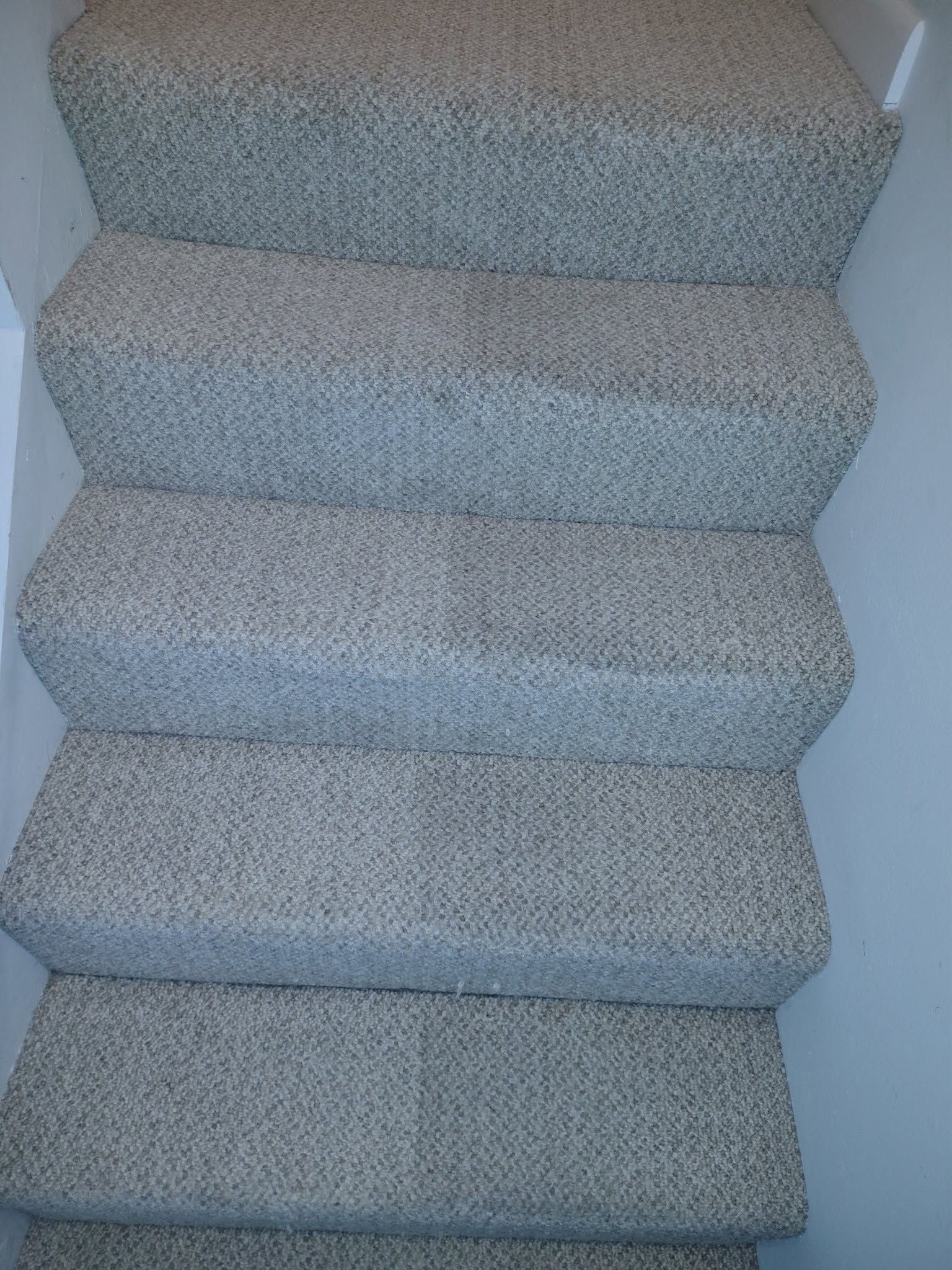 Carpeted indoor staircase with light gray steps and white walls on either side