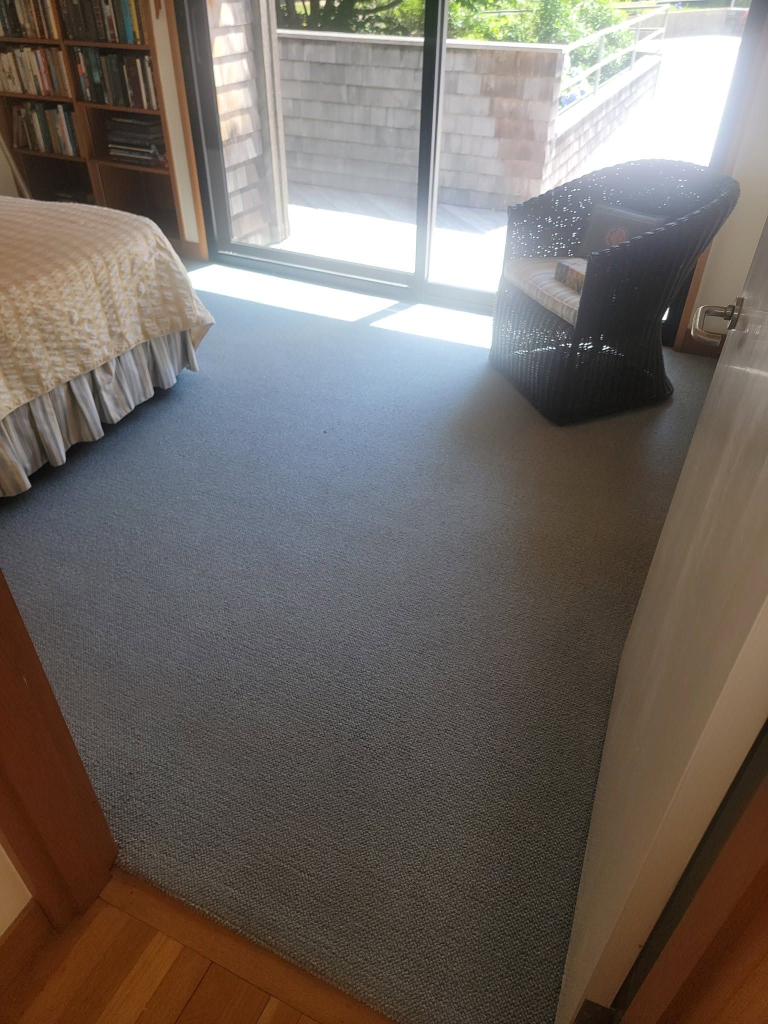 Carpeted bedroom opening to a sliding glass door, with a chair by the window and a bed on the left.