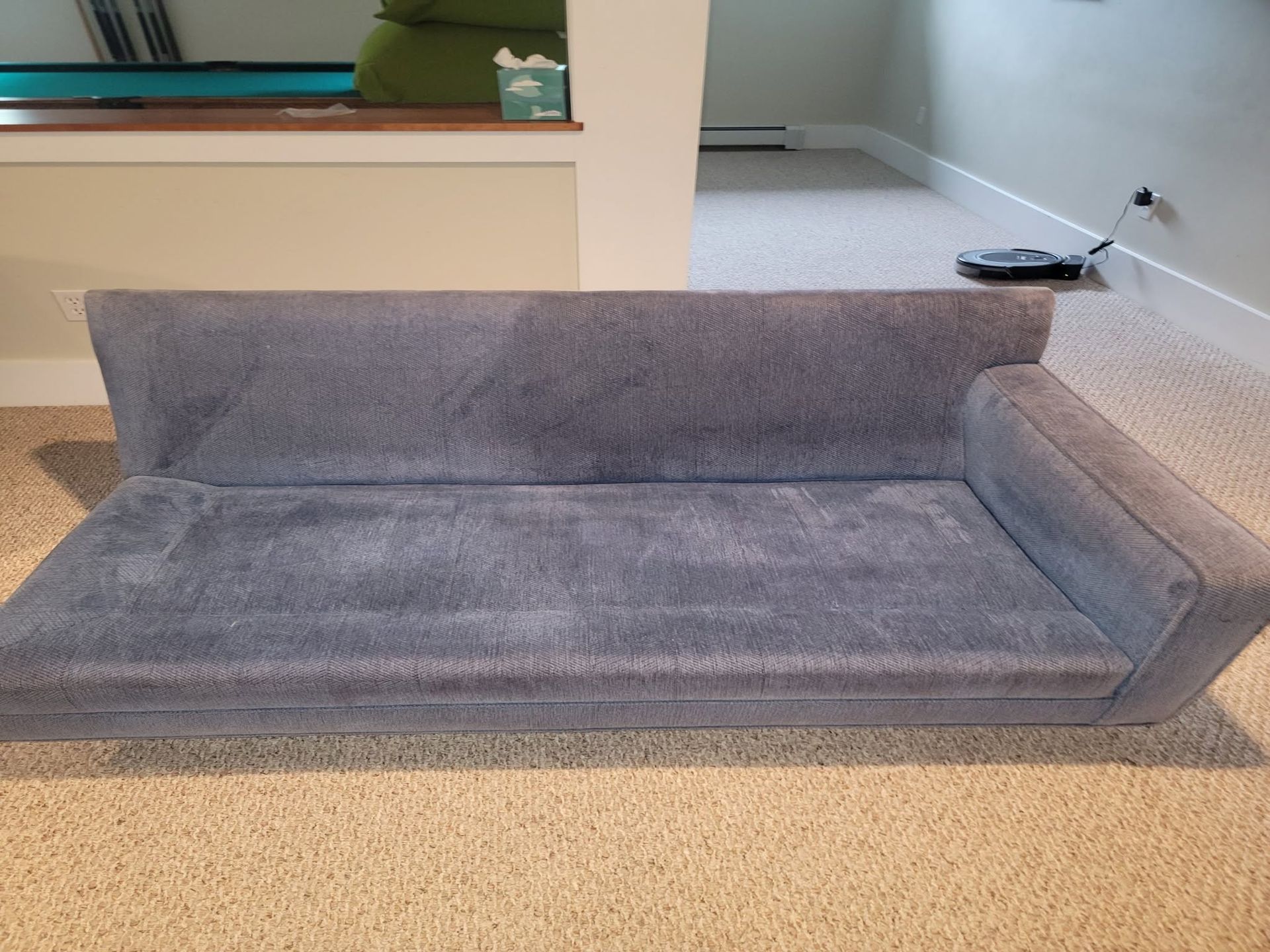 Gray fold-out sofa bed on beige carpet in a living room.