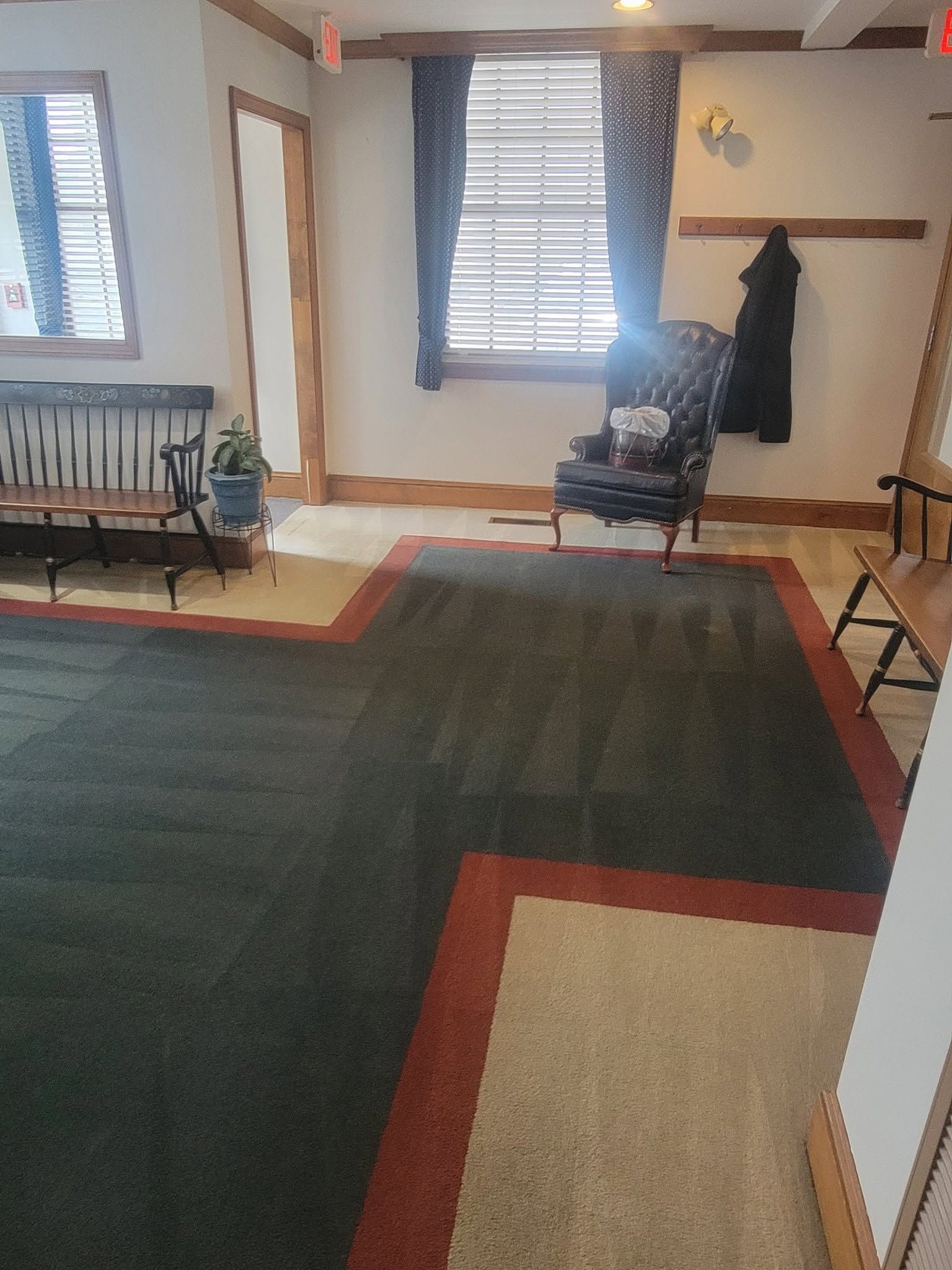 Living room with dark rug, two windows, chair, coat rack, and bench along the walls