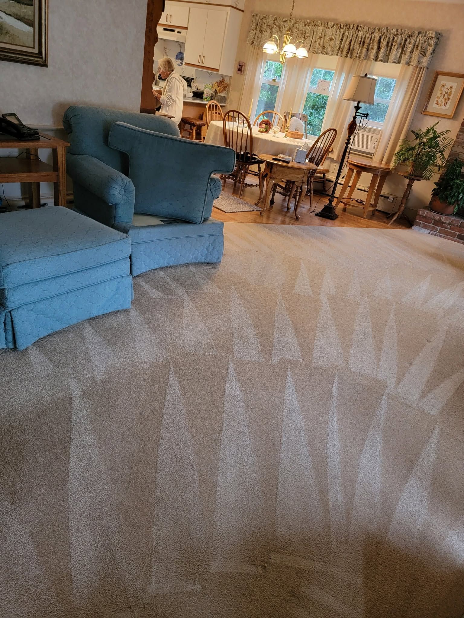 Cozy living room with blue armchair, beige carpet, and dining area by sunlit windows