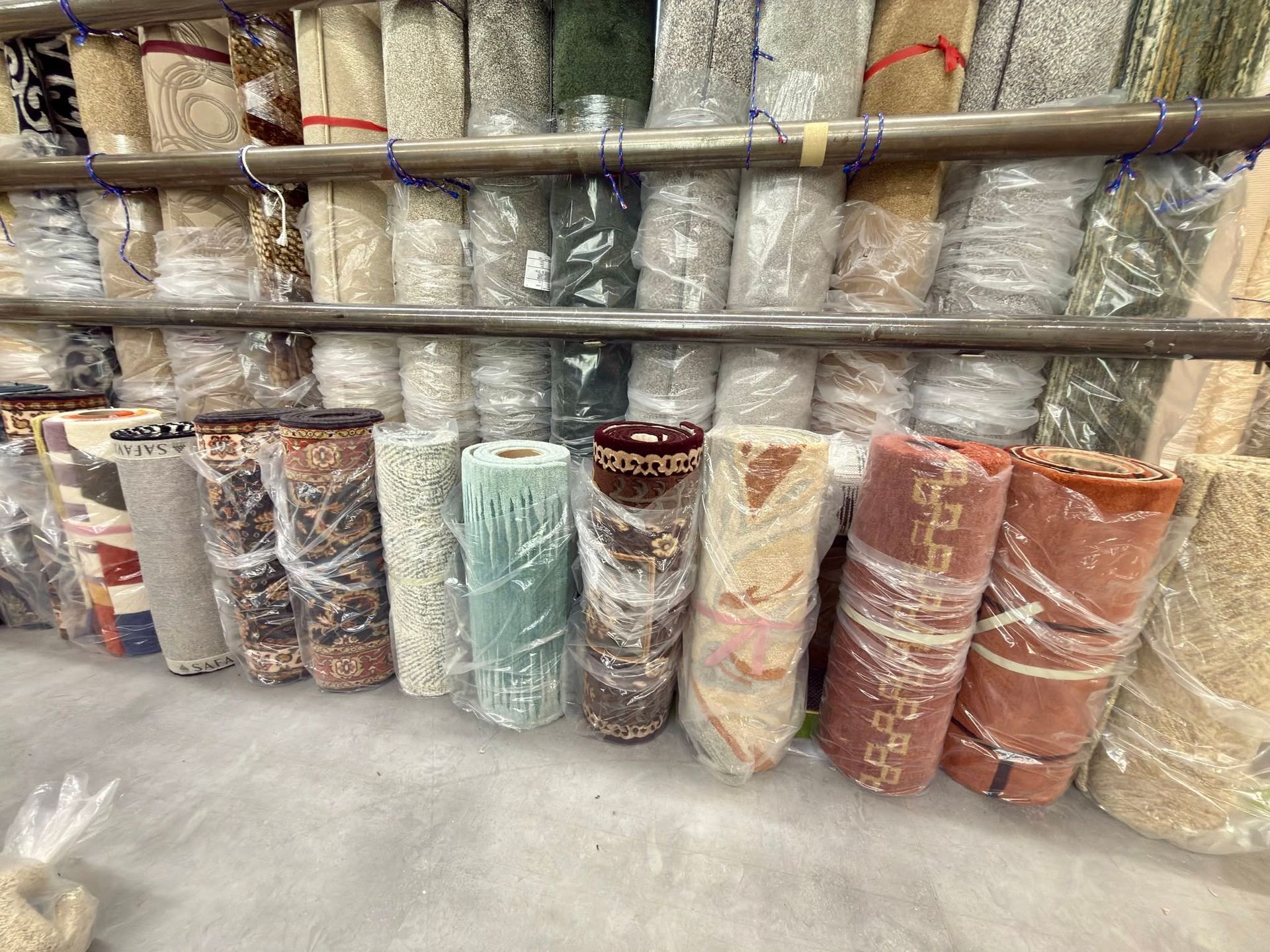 Rolled rugs wrapped in plastic stacked on shelves in a carpet warehouse