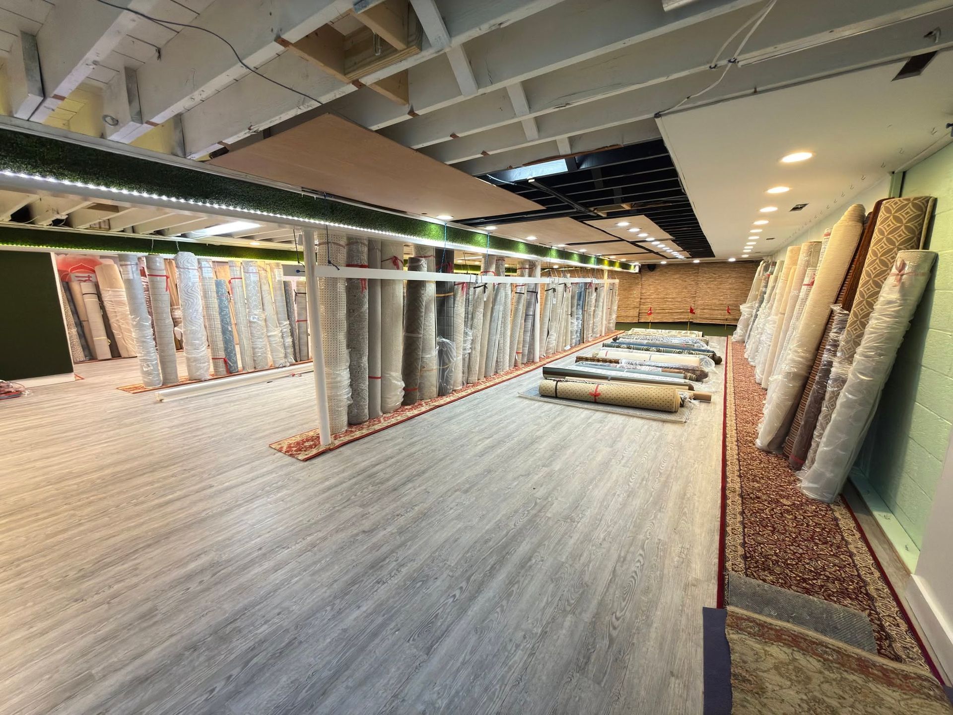 Carpet showroom with rows of rolled rugs and hanging samples under bright ceiling lights.