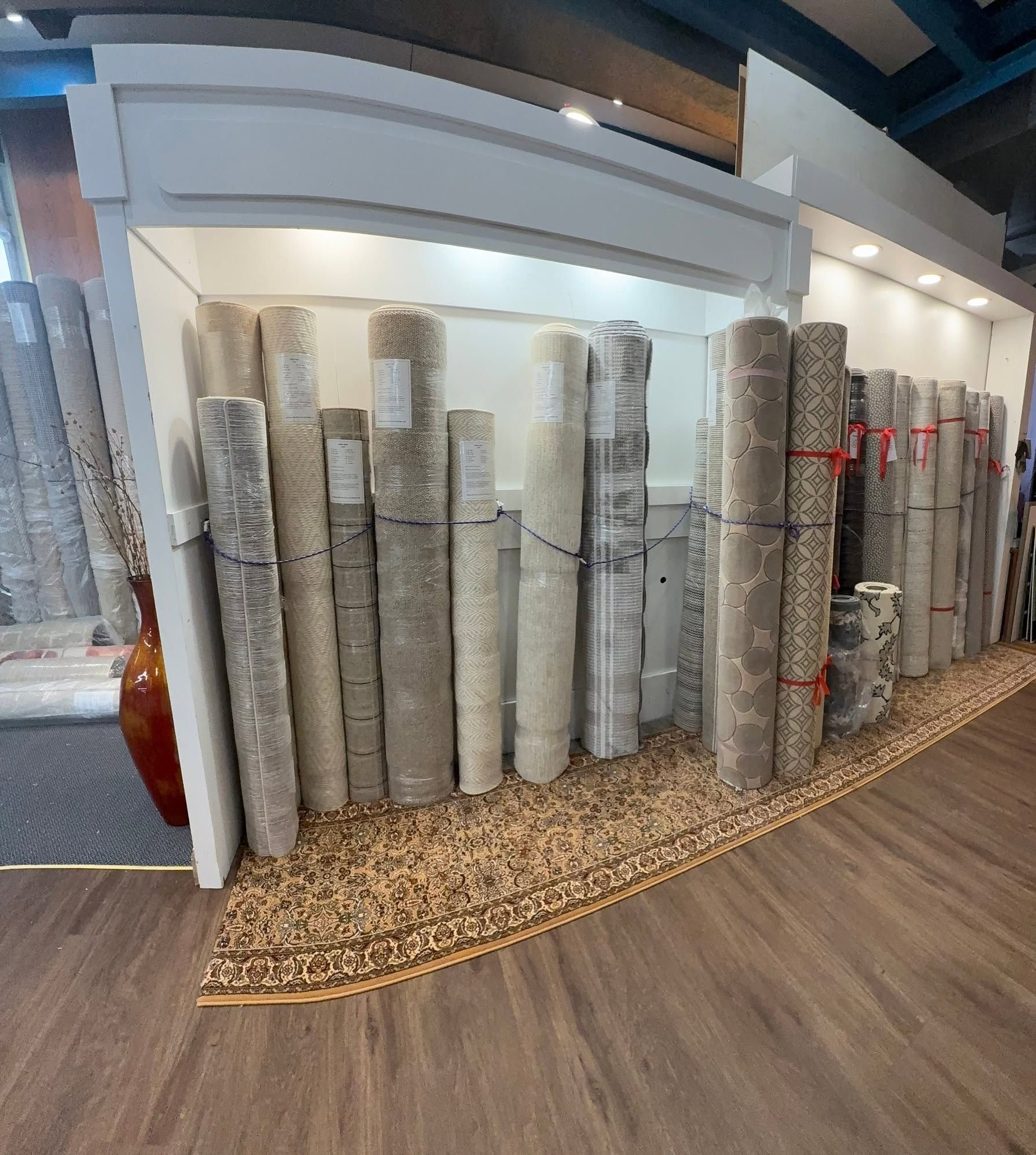 Rolled carpets displayed in a showroom, stacked along a wall on a curved rug border.