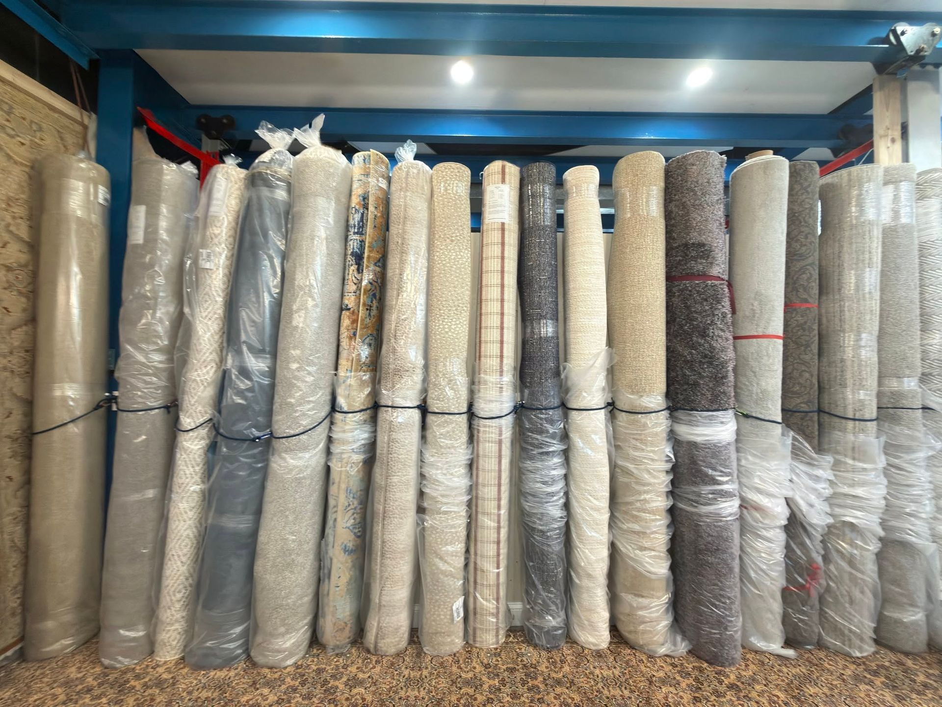 Rolled carpets and rugs stacked upright in a storage room, wrapped in plastic and plastic netting.