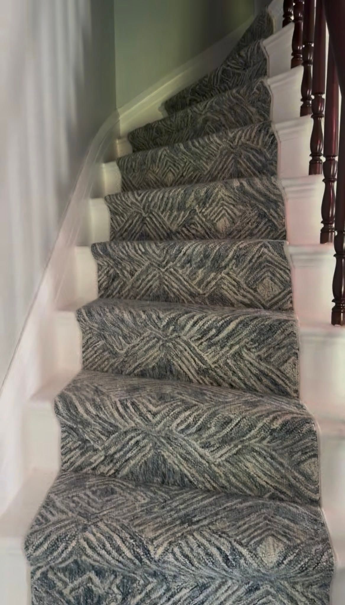 Narrow carpeted staircase with patterned runner, white walls, and dark wooden banister.