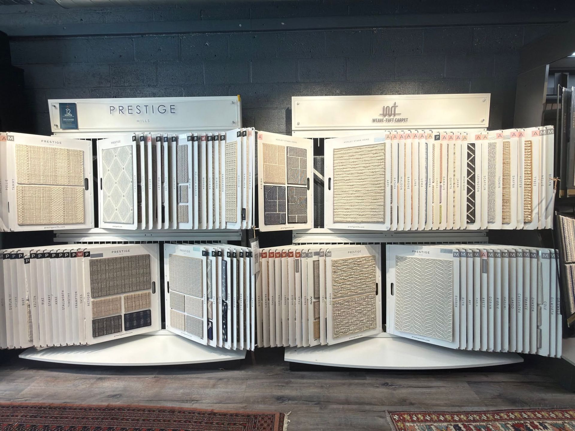 Display of carpet samples in a showroom, arranged on shelves with white sample boards and color swatches.