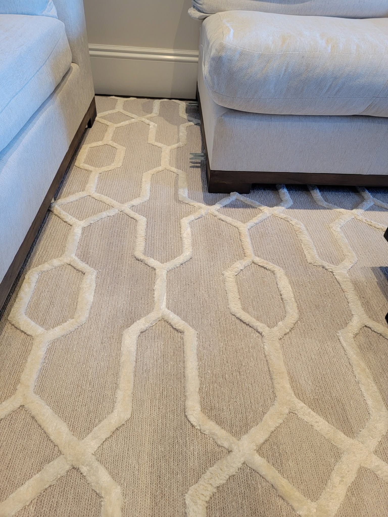 Light gray patterned rug between two beige sofas in a living room