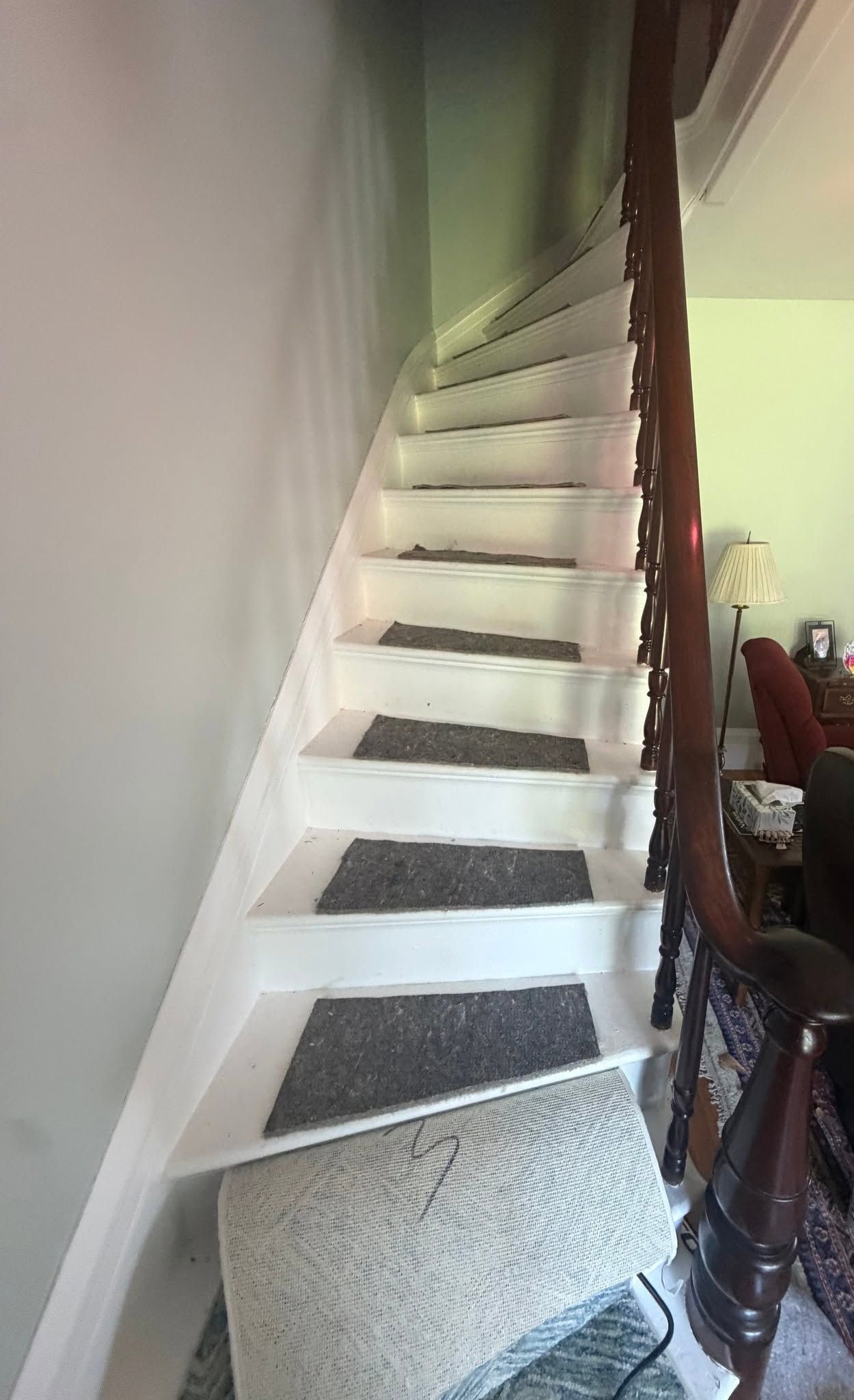 Narrow indoor staircase with white steps and gray carpet runners beside a wall and railing