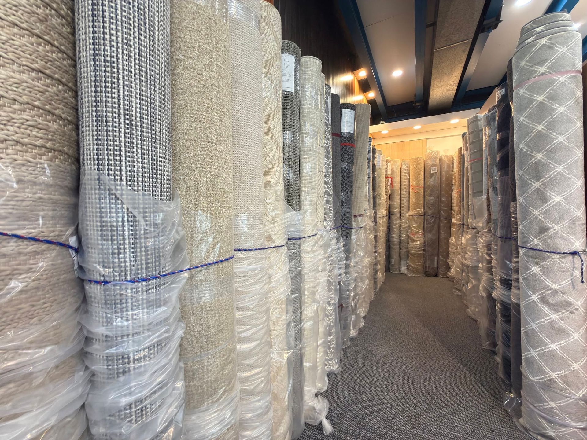 Narrow storage aisle lined with wrapped rolls of carpet or insulation under warm lights