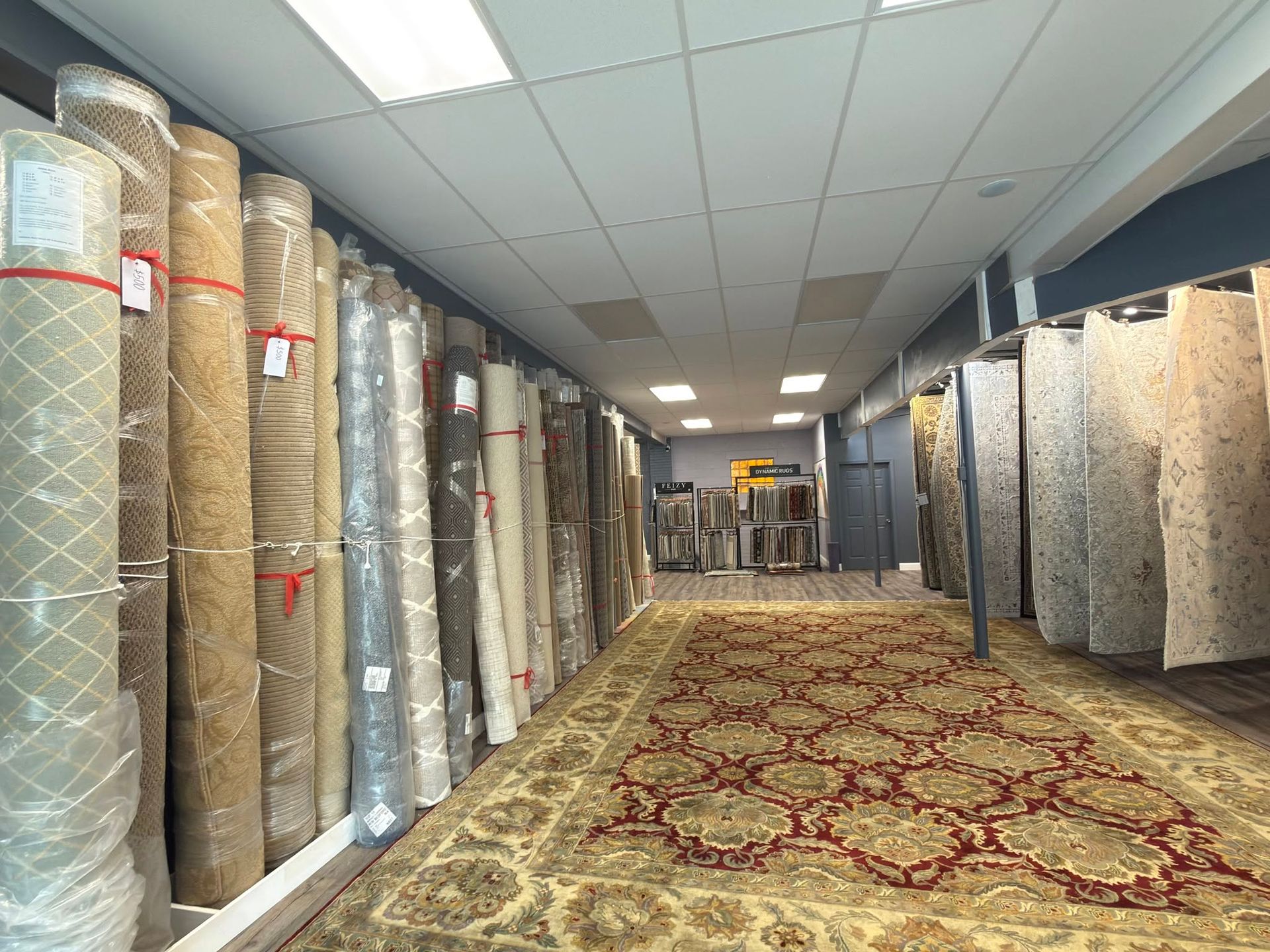 Carpet showroom aisle lined with rolled rugs on both sides and a patterned carpet runner down the center