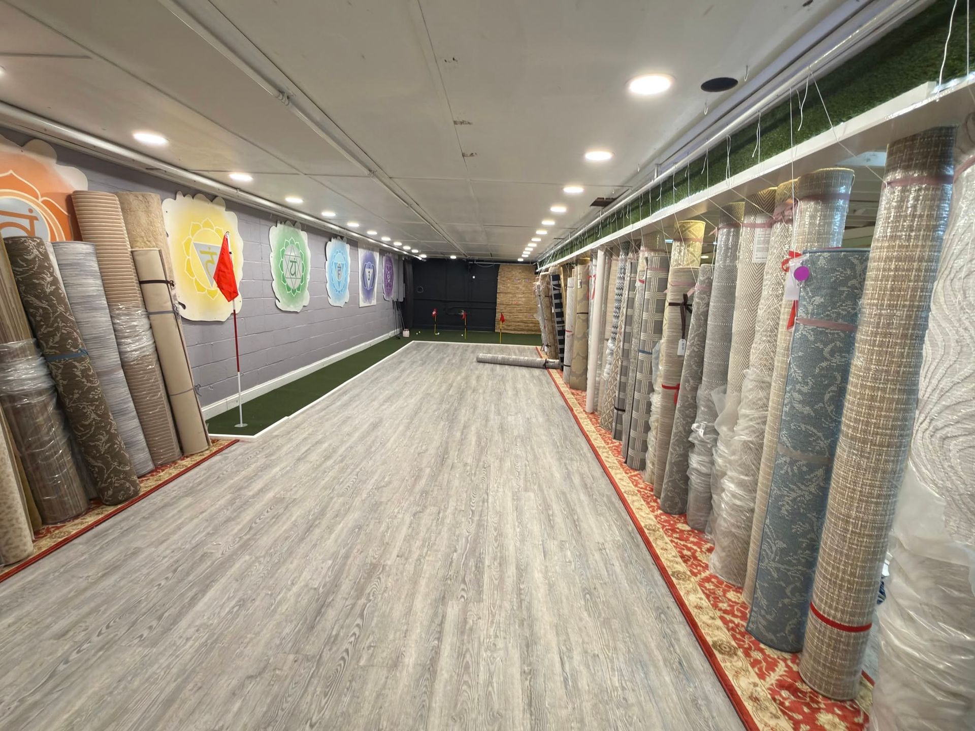 Carpet showroom aisle lined with rolled rugs and wall-mounted samples under bright ceiling lights