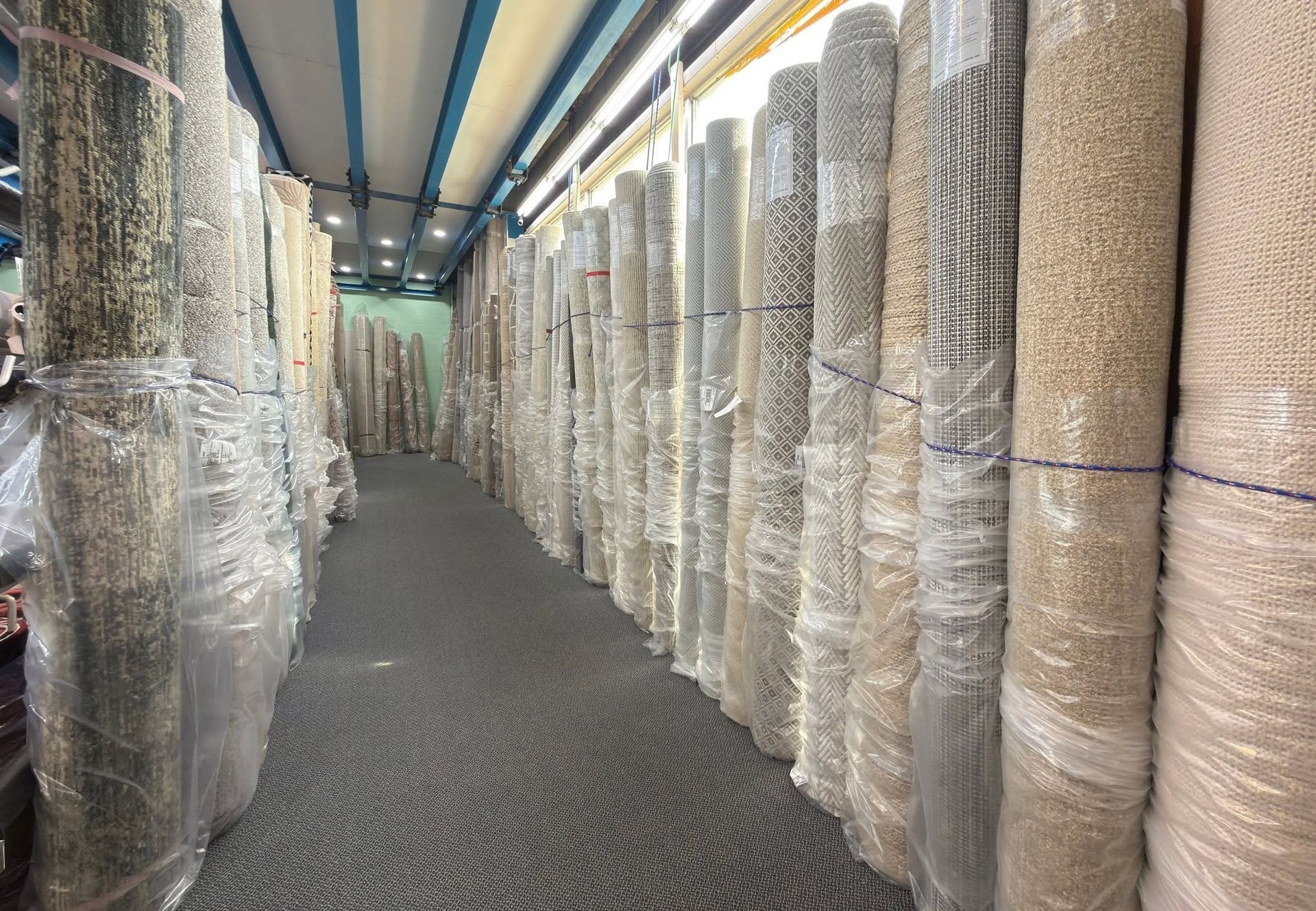 Aisle in a warehouse lined with stacked rolls of carpet wrapped in plastic.