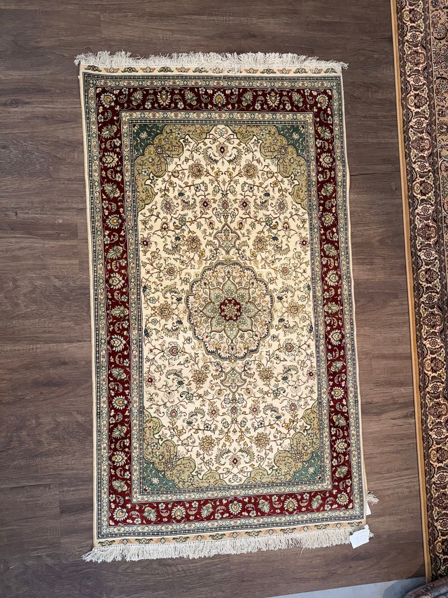 Small ornate cream and red patterned rug on a gray floor, viewed from above