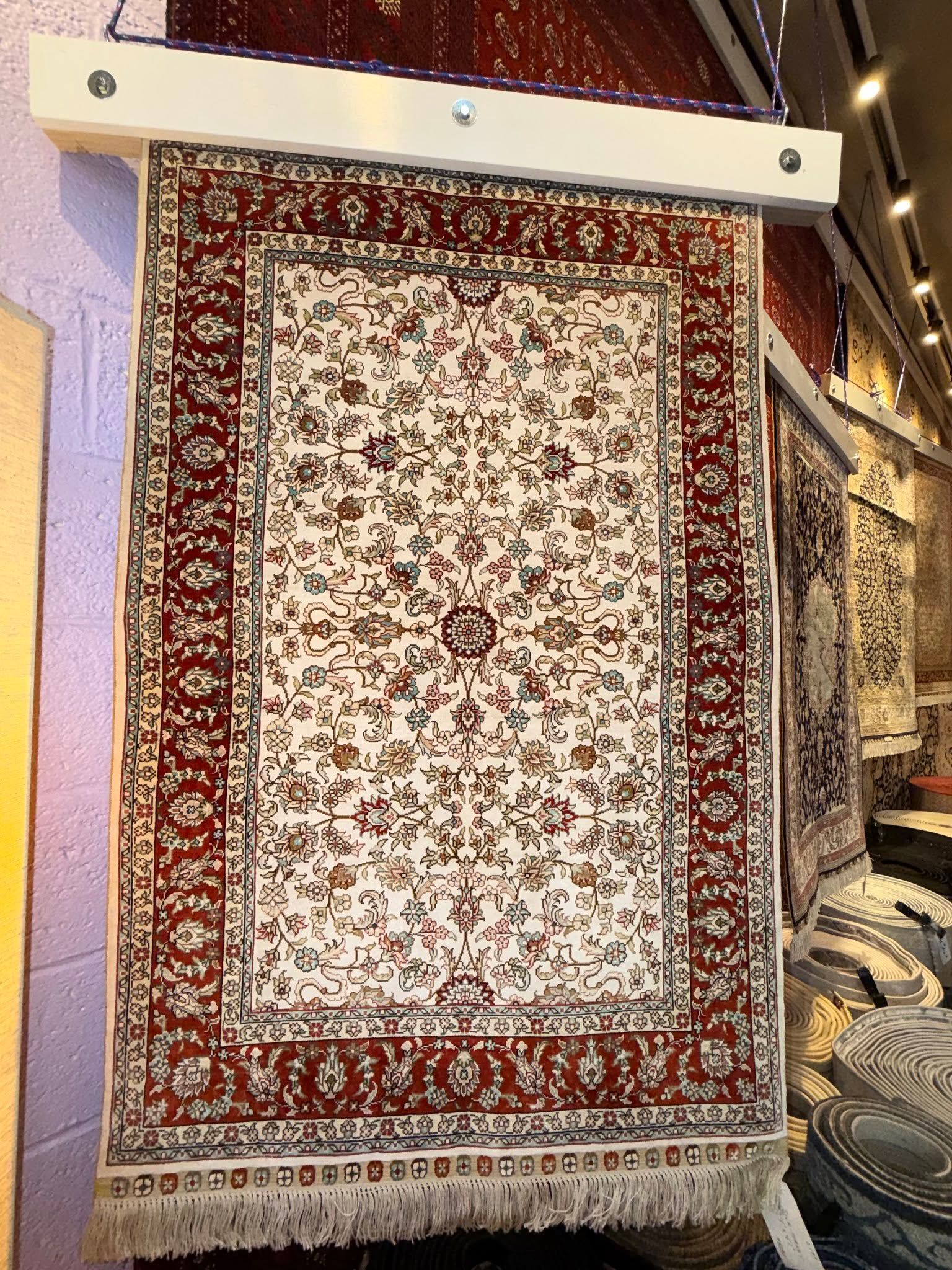 Red and cream patterned rug hanging vertically on display indoors.