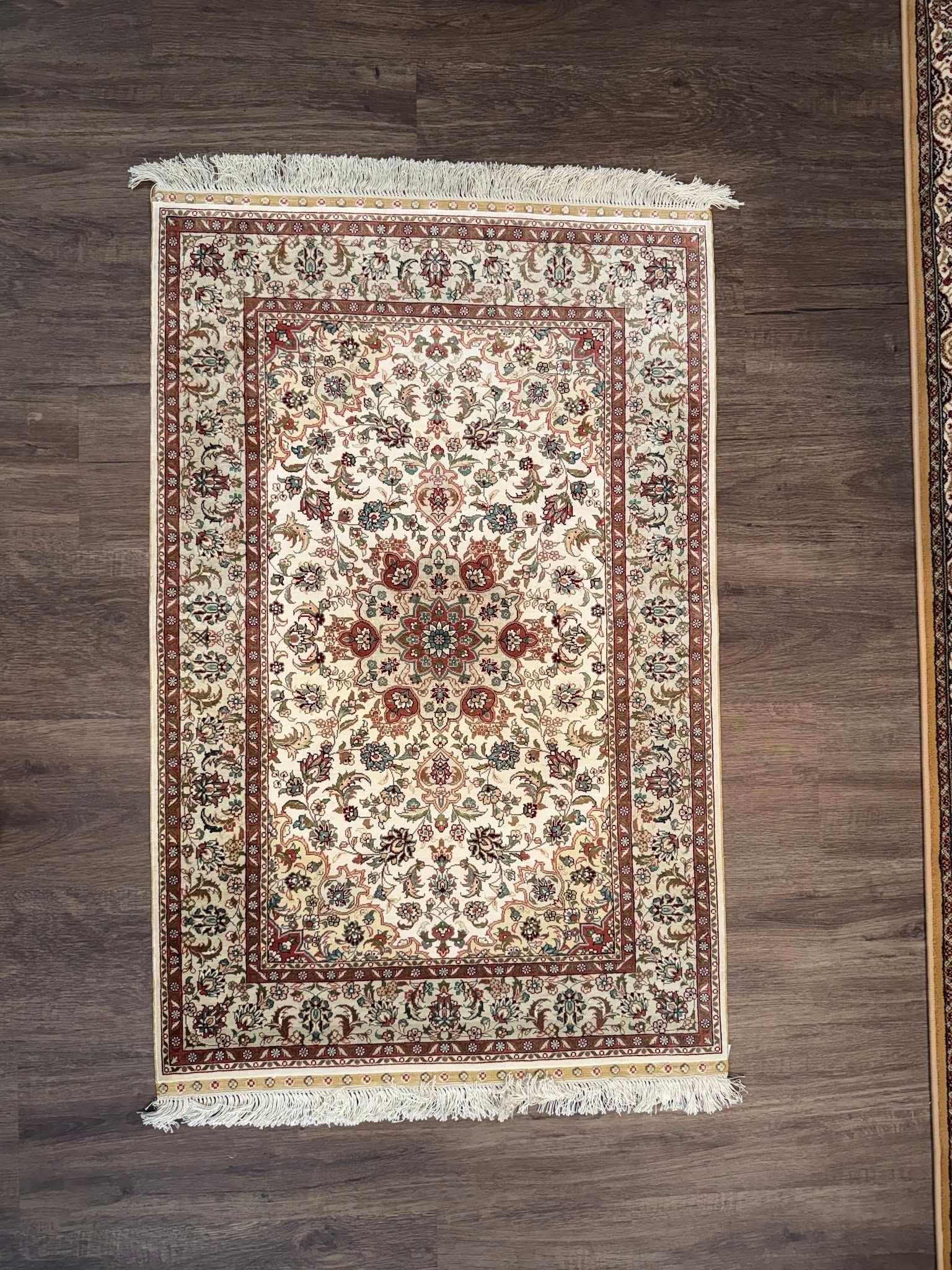 Beige and red patterned rug with fringe, laid on a dark wooden floor.