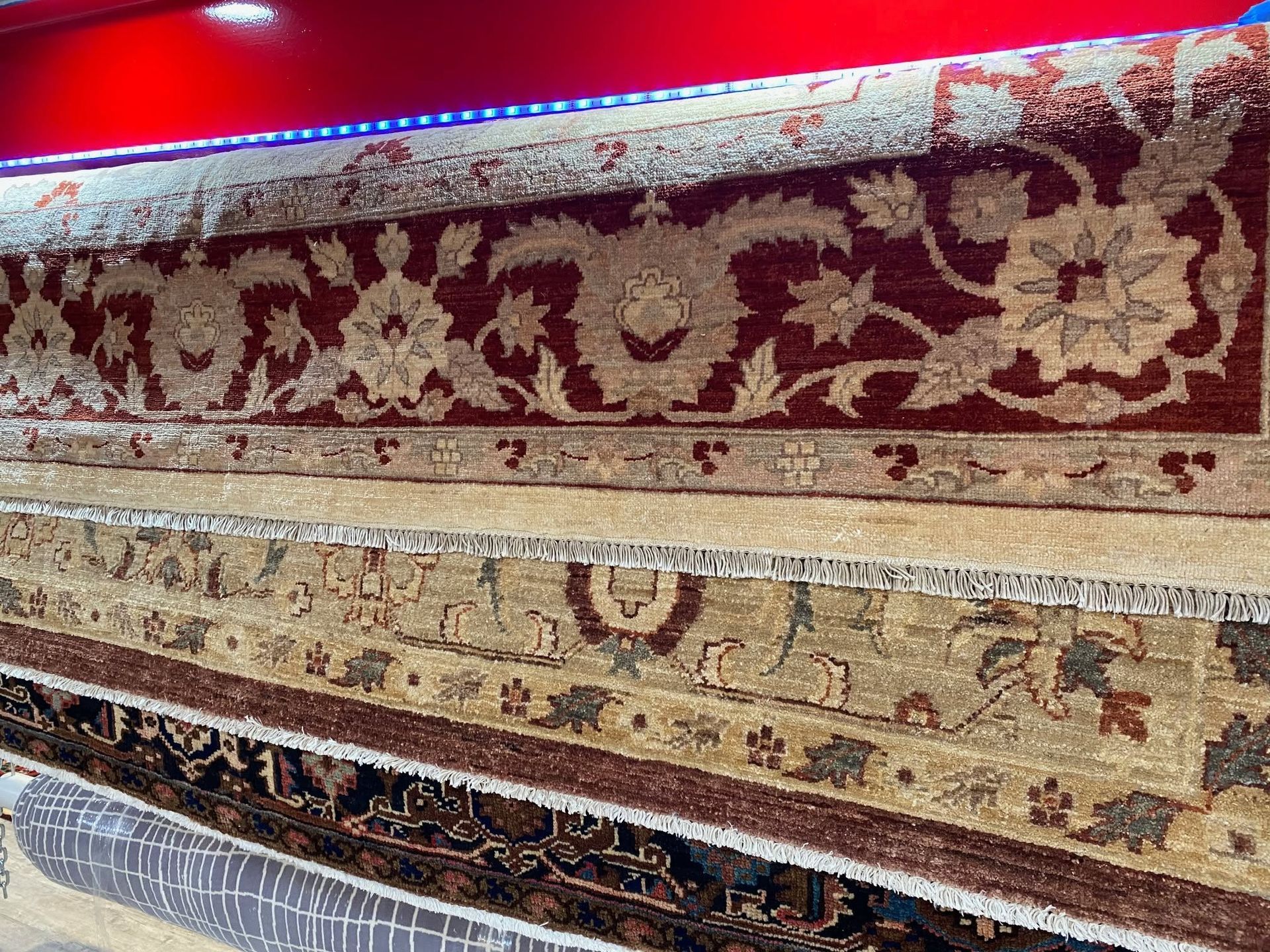 Stacked ornate patterned rugs displayed in a store with a bright red wall behind them