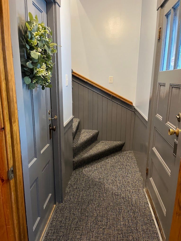 Narrow hallway with carpeted steps, gray walls, and decorated front doors on both sides.