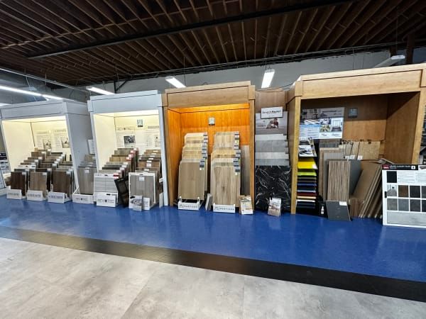 Flooring display showroom with sample racks and wood, tile, and carpet displays along a blue carpeted aisle