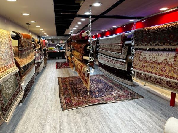 Rug showroom aisle with patterned carpets displayed on both walls and floor under warm lighting