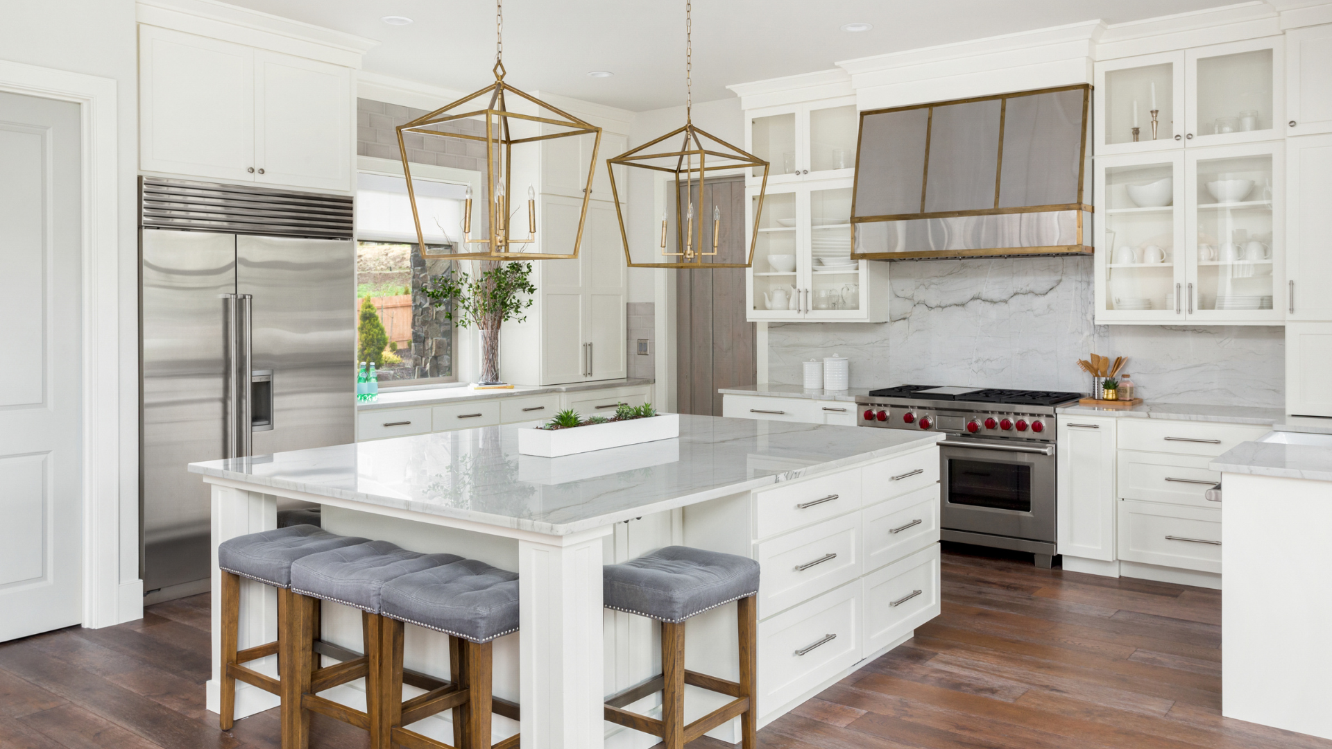 Bright modern kitchen with white cabinets, marble island, gold pendant lights, and wood floors