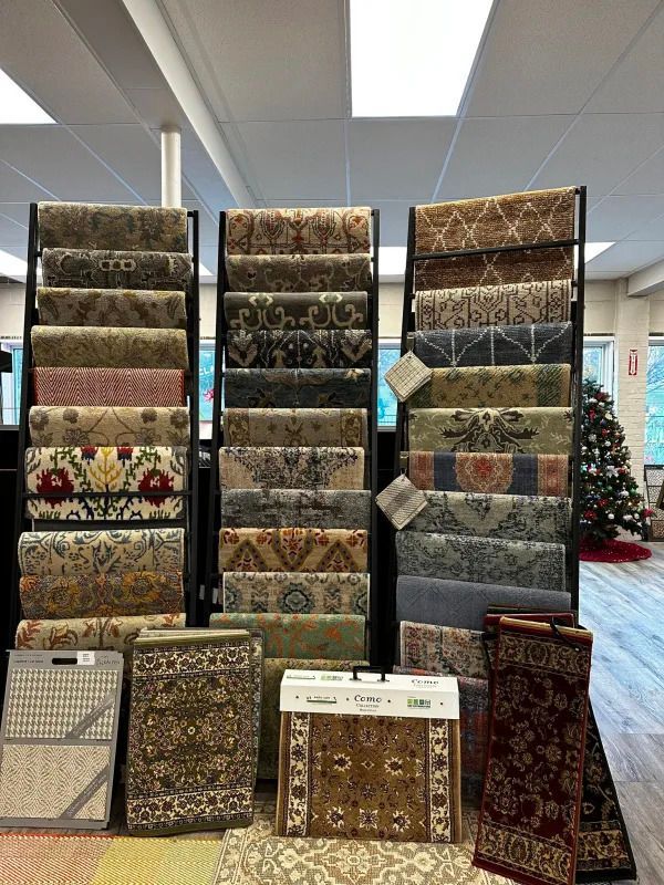 Carpet display in a store, with several patterned rugs on racks and a Christmas tree in the background
