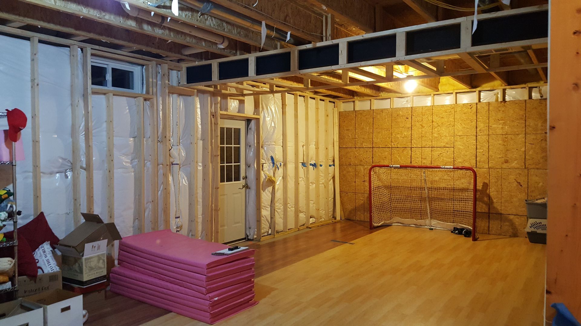 A basement under construction with a hockey net and a stack of pink mats.
