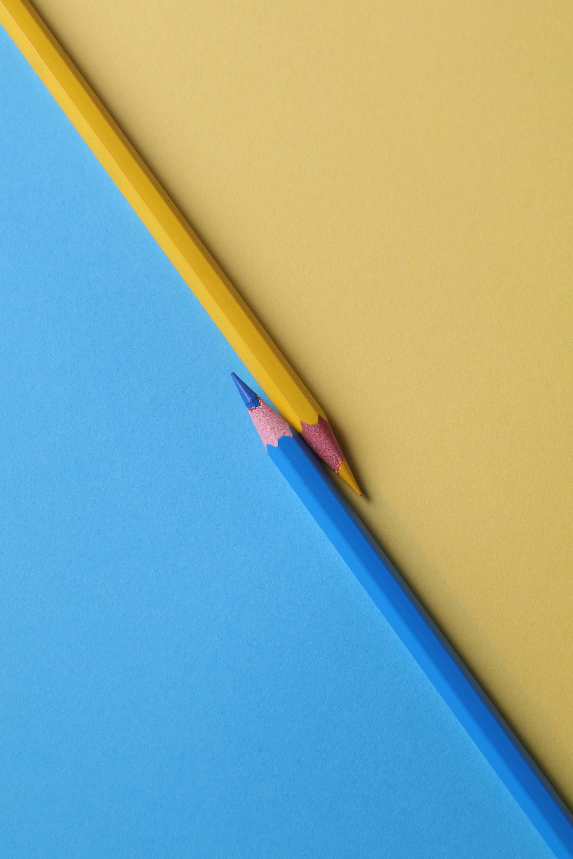 Yellow and blue pencils on yellow and blue paper, crossing each other.