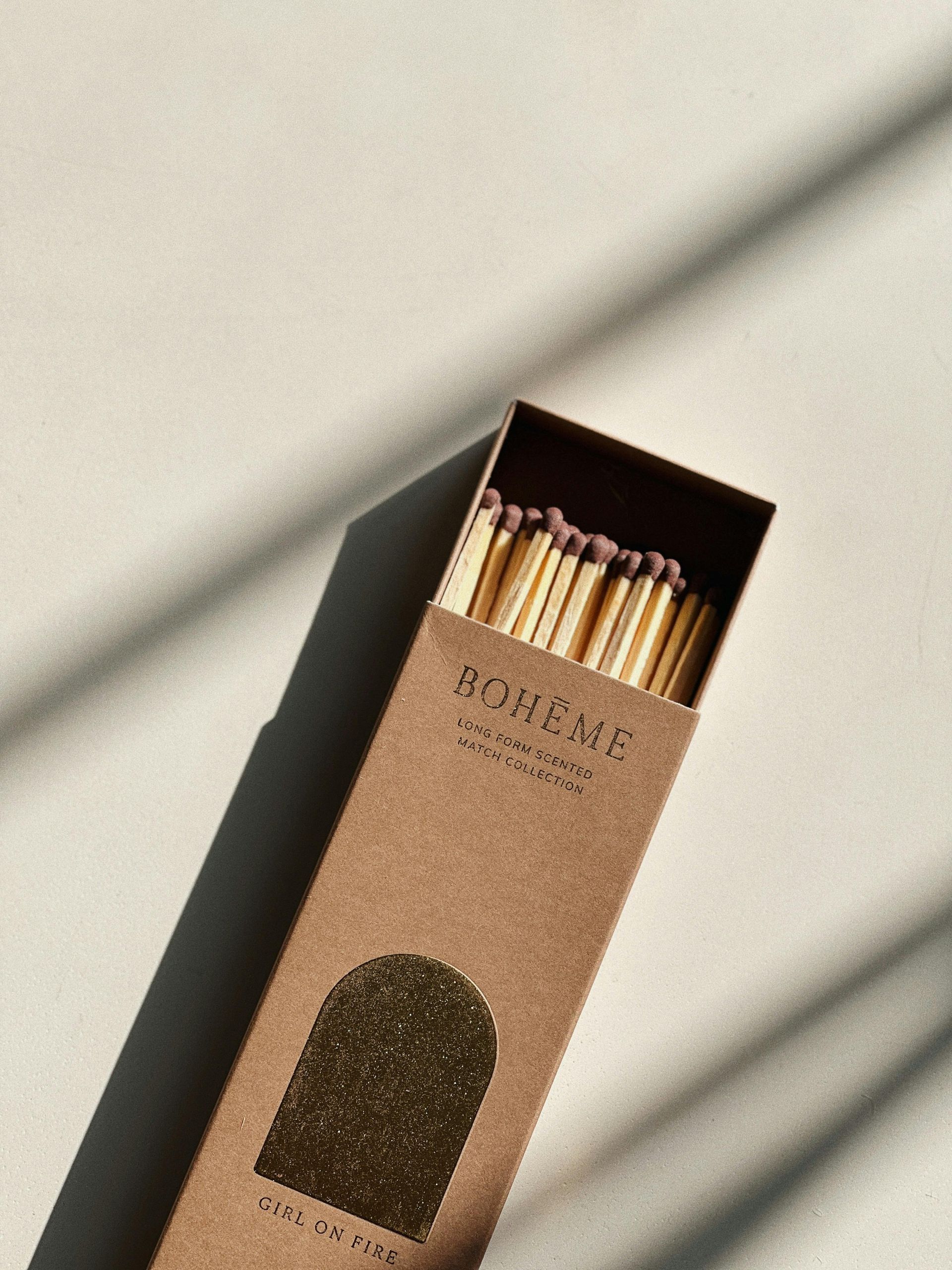 Box of matches, gold foil details, brown box, match heads visible, against a light background with shadows.