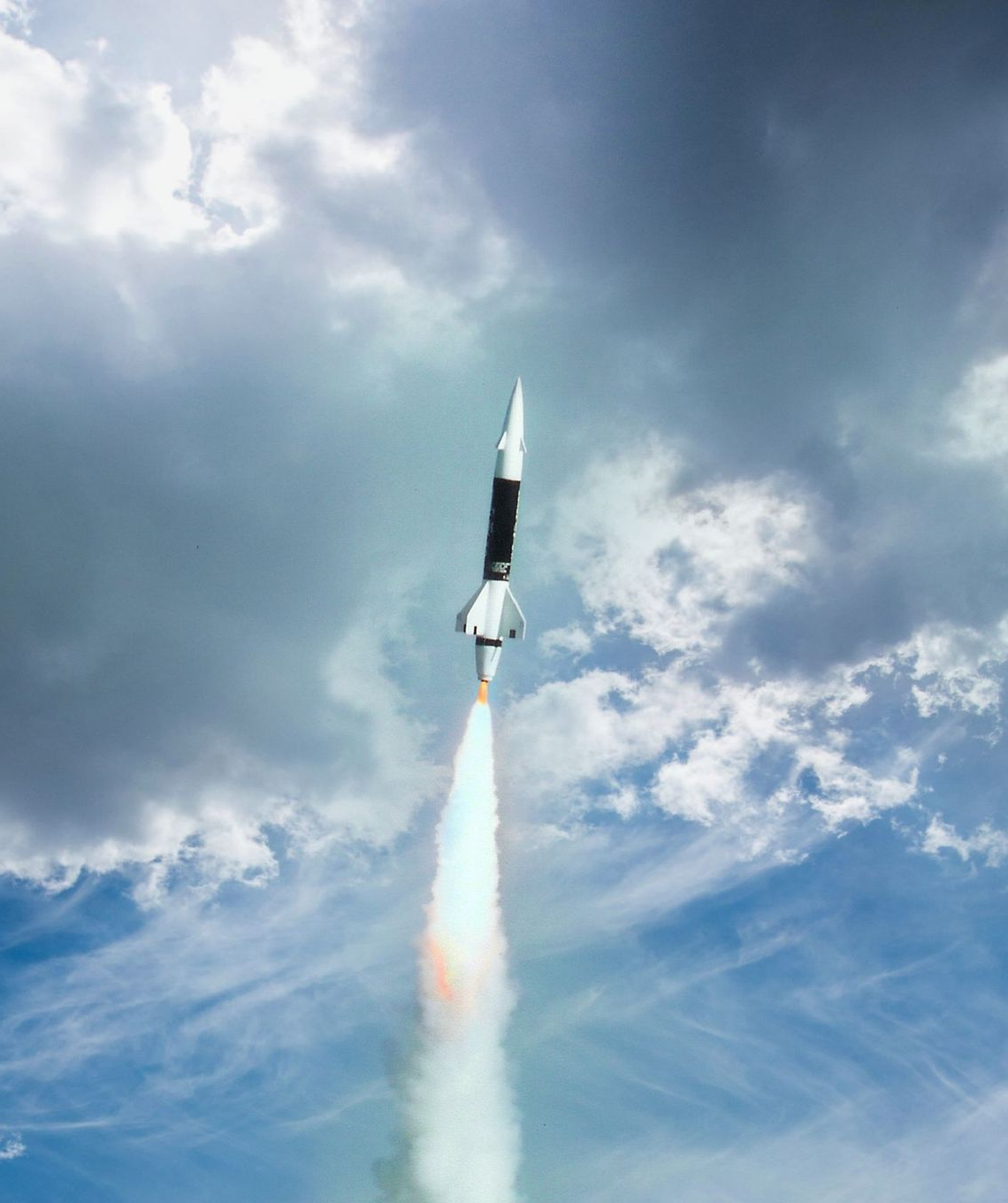 Rocket launching into a cloudy blue sky, leaving a bright exhaust plume behind.