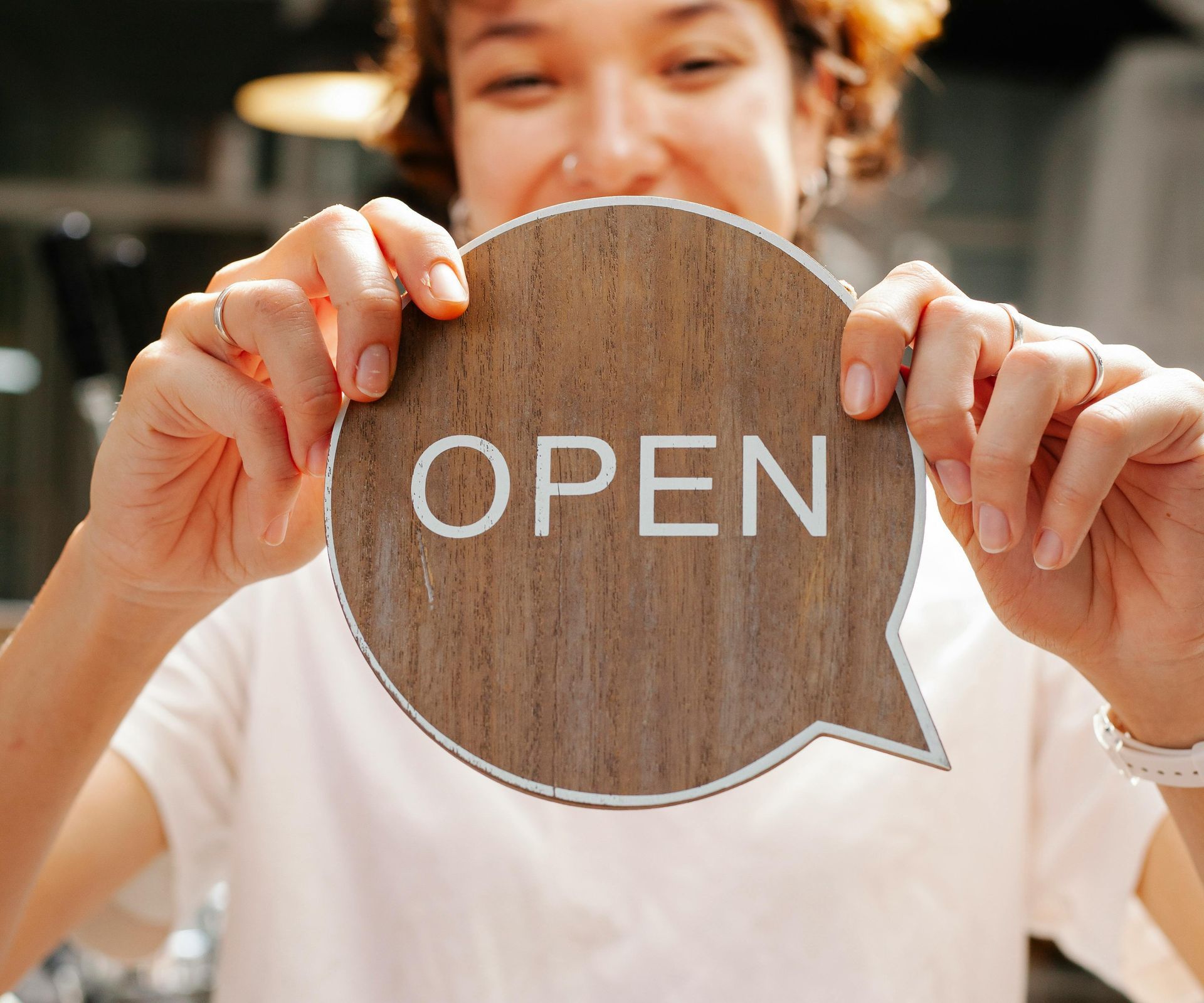 Person holding a round wooden sign that says “OPEN” in front of a storefront